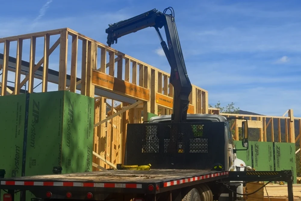 Crane truck extending its boom over a framed wall during steel ceiling beam placement