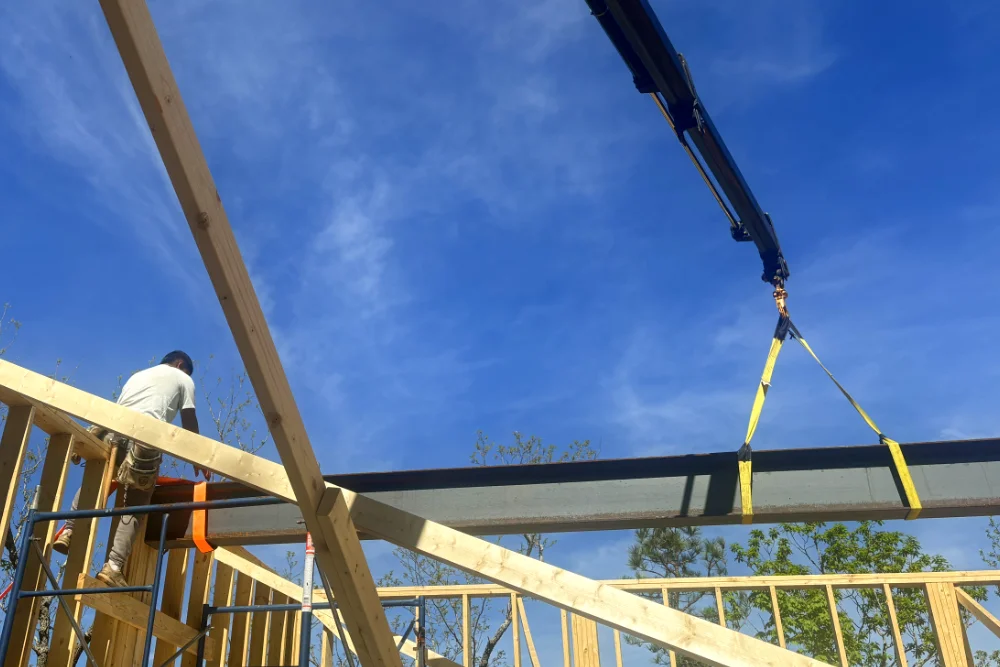 Steel I-beam rigged with two 13,000-lb web slings being lifted by a knuckleboom crane